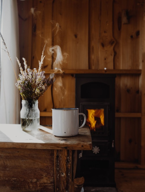 Ambiente com paredes e mesa de madeira, uma xícara de café em cima da mesa e um vaso de flores. 